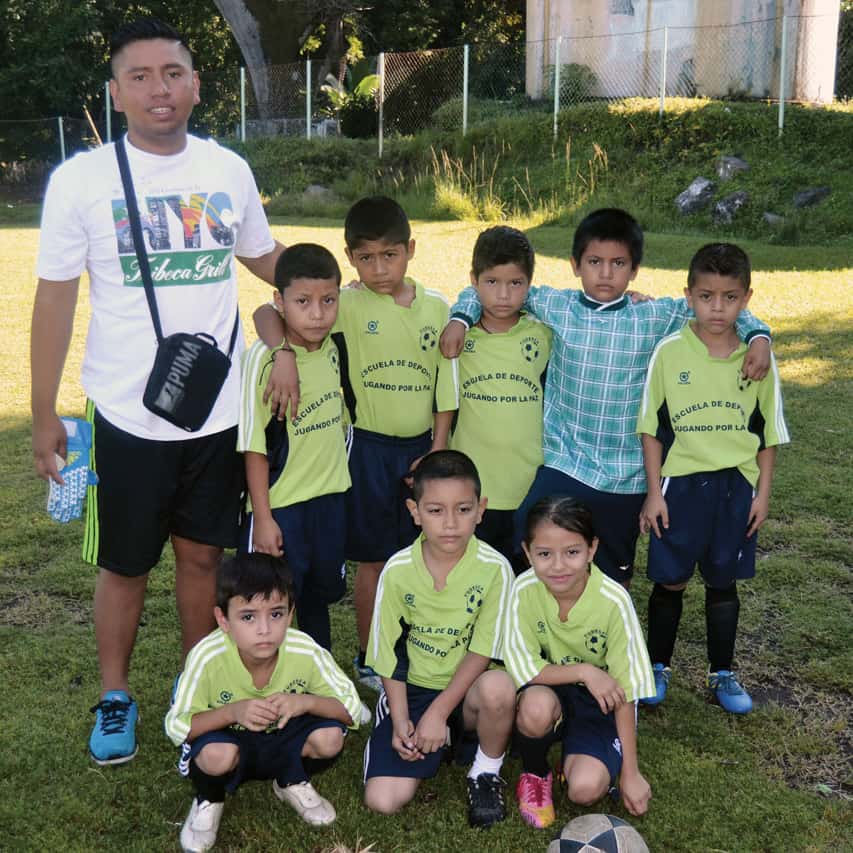 Coach Juan Moreno stand with eight little soccer players in the El Salvadoran community of Las Delicias.