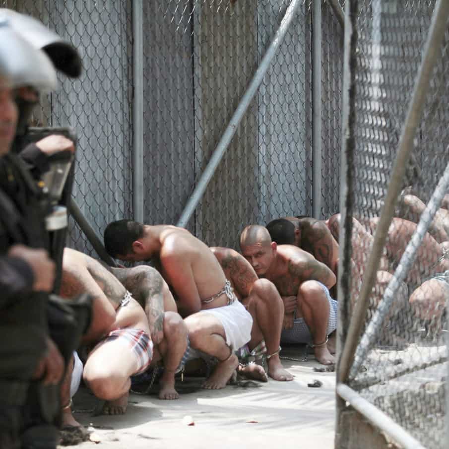 Shirtless members of the Mara Salvatrucha gang crouch under the eye of police in El Salvador.