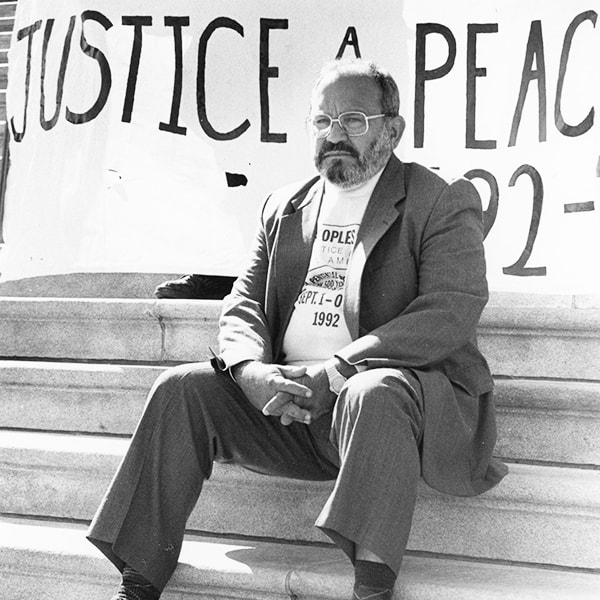 The missionary d'Escoto seated in front of a banner that reads: Justice and Peace People in Washington D.C. in 1992.