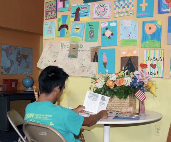 A boy seated at a table and facing a wall reads a welcome greeting card the day he arrives at Annunciation House, a migrant shelter in El Paso.