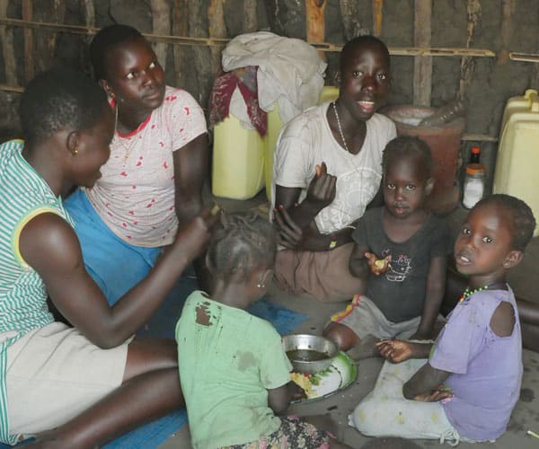 Refugee mothers and children of the Acholi tribe from South Sudan eat lunch in a tukul, a typical mud and thatch hut of East Africa, at the Palabek Refugee Settlement.