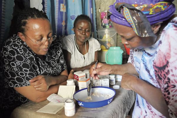 Alice Njoroge, left, managing director of HIV AIDS relief program known as EDARP, observes the counting of medicine by a community health worker at the home of a beneficiary in Nairobi.