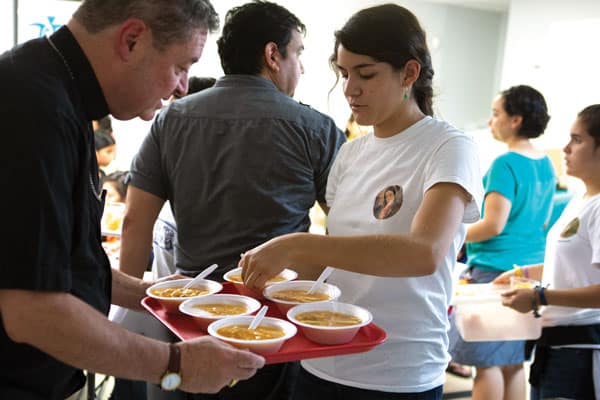 Visiting U.S.-Mexico border, Bishop Robert Brennan of Rockville Centre, N.Y., helps a volunteer serve soup to separated migrants just released from detention. (CNS/C. Muth/U.S.)