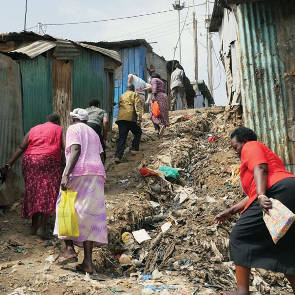 Community health workers with EDARP, an HIV AIDS relief program, trudge up a steep trash-filled dirt byway en route to see clients in the Mathare slum in Nairobi.