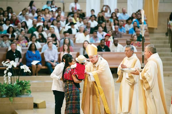 Former undocumented immigrant helps migrants today in Los Angeles: Archbishop José H. Gomez of Los Angeles blesses a family from Guatemala at a Mass celebrated in recognition of all immigrants. (Archdiocese of Los Angeles/Victor Aleman)
