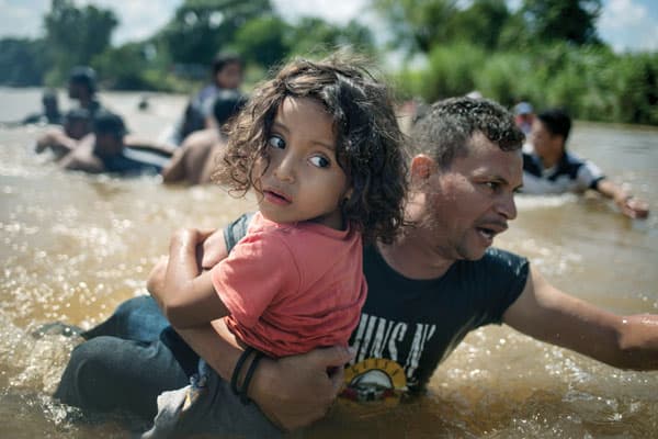 Former undocumented immigrant helps migrants today in Los Angeles: In a caravan of migrants from Central America to the United States, a man carries a child through the Suchiate River into Mexico from Guatemala. (CNS/A. Latif, Reuters)