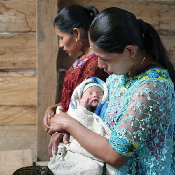 Wearing her native dress, a Q'eqchi' Mayan villager cradles her infant as she prays at Mass. (Sean Sprague)