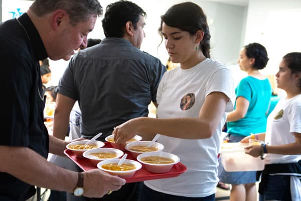 Reflection: With Refugees in El Paso- Bishop Robert J. Brennan, auxiliary bishop of Rockville Centre, N.Y., helps a volunteer at a Catholic Charities-run respite center in McAllen, Texas, serve soup July 1, 2018, to immigrants recently released from U.S. custody. A delegation of U.S. bishops has traveled to the Diocese of Brownsville, Texas, to learn more about the detention of Central American immigrants at the U.S.-Mexican border. (CNS photo/Chaz Muth