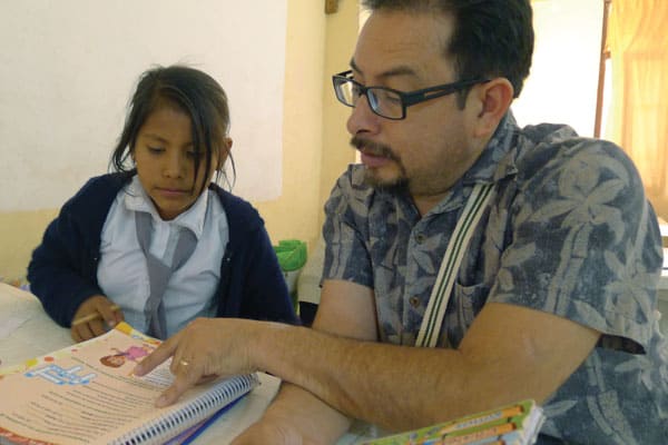 Deacon Leonel Yoque helps a little girl with homework at Apoyo Escolar program. Yoque, who is a member of the Maryknoll Discípulos Misioneros (Missionary Disciples) team, which sponsored the Maryknoll immersion trip to Bolivia. Photo by D. Aquije/Bolivia.