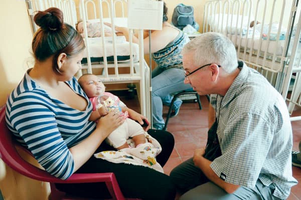 While visiting the national hospital during Maryknoll mission immersion trip to El Salvador, Deacon Kevin McCarthy comforts a mother holding her sick child. Photo by S. Sprague/El Salvador