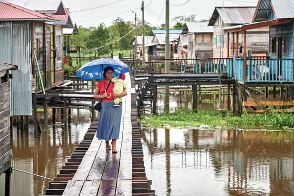 Carrying a child, a woman walks along a raised sidewalk in Islandia, a town in the Peruvian Amazon. The Amazon Synod at the Vatican in October address various issues, including the environmental threat to the forest and ministry to the Amazonian people.(CNS/Paul Jeffrey/Peru)