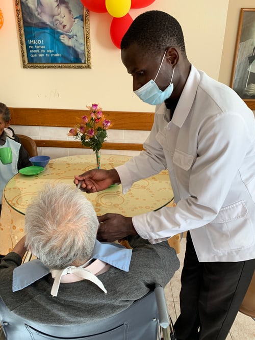 Wearing a face mask Charles Ogony, a Maryknoll seminarian from Kenya, feeds a resident at a senior home run by the Little Sisters of the Abandoned Elderly in Cochabamba, Bolivia. Ogony and fellow seminarian Matthew Sim helped out at the home after volunteers were withdrawn due to the Covid-19 pandemic. (Matthew Sim/Bolivia)