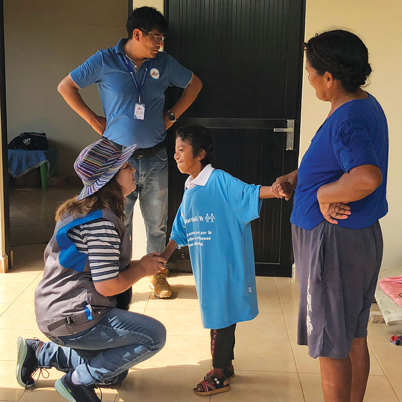 Siles shares a tender moment with Jhon Alex Muñoz as his mother, Doña Benita, looks on. Thanks to physical therapy, Jhon Alex can now walk. (Meinrad Scherer Emunds/Bolivia)